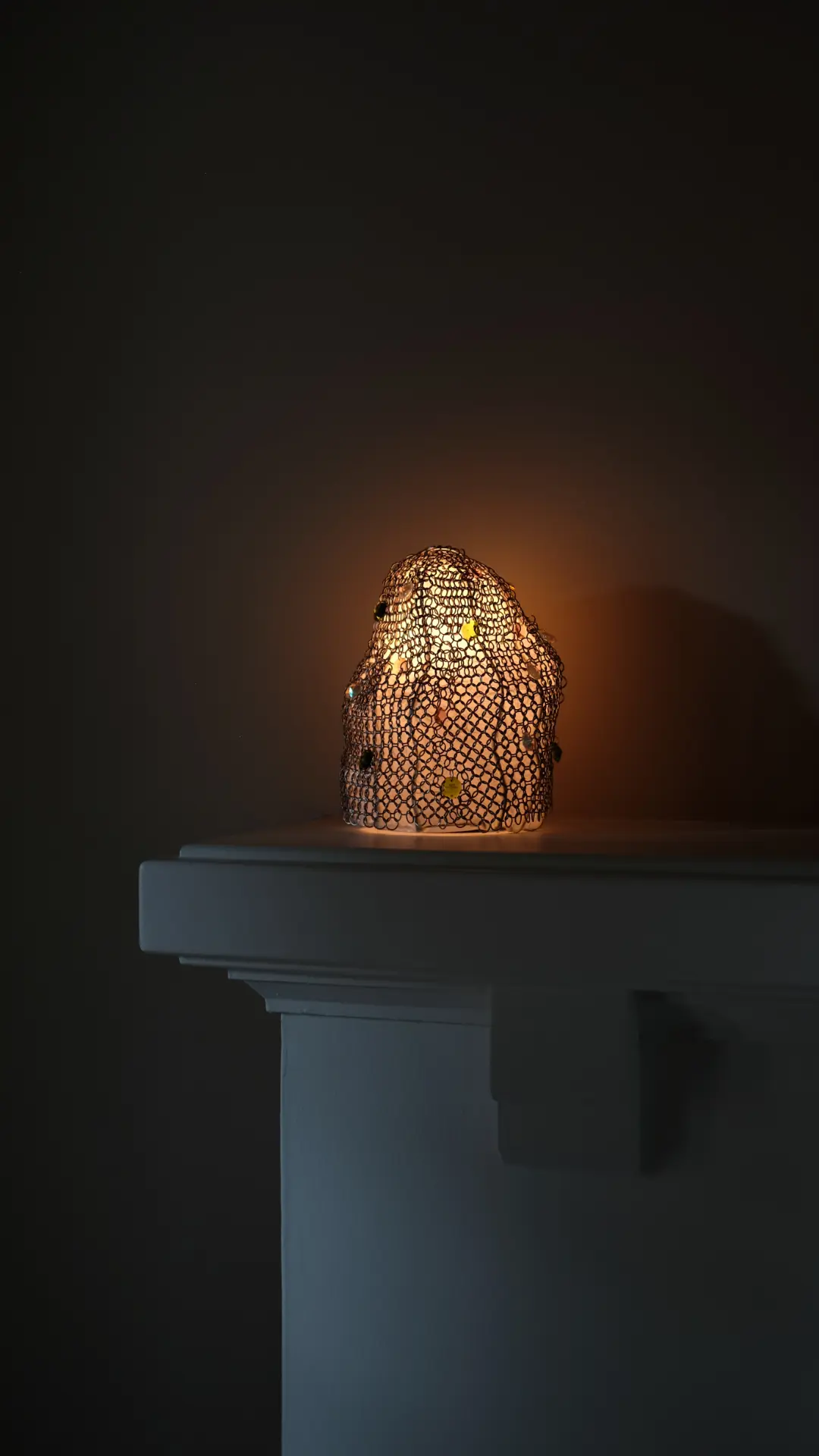 The completed chainmail lamp, illuminated, on a stone plinth.