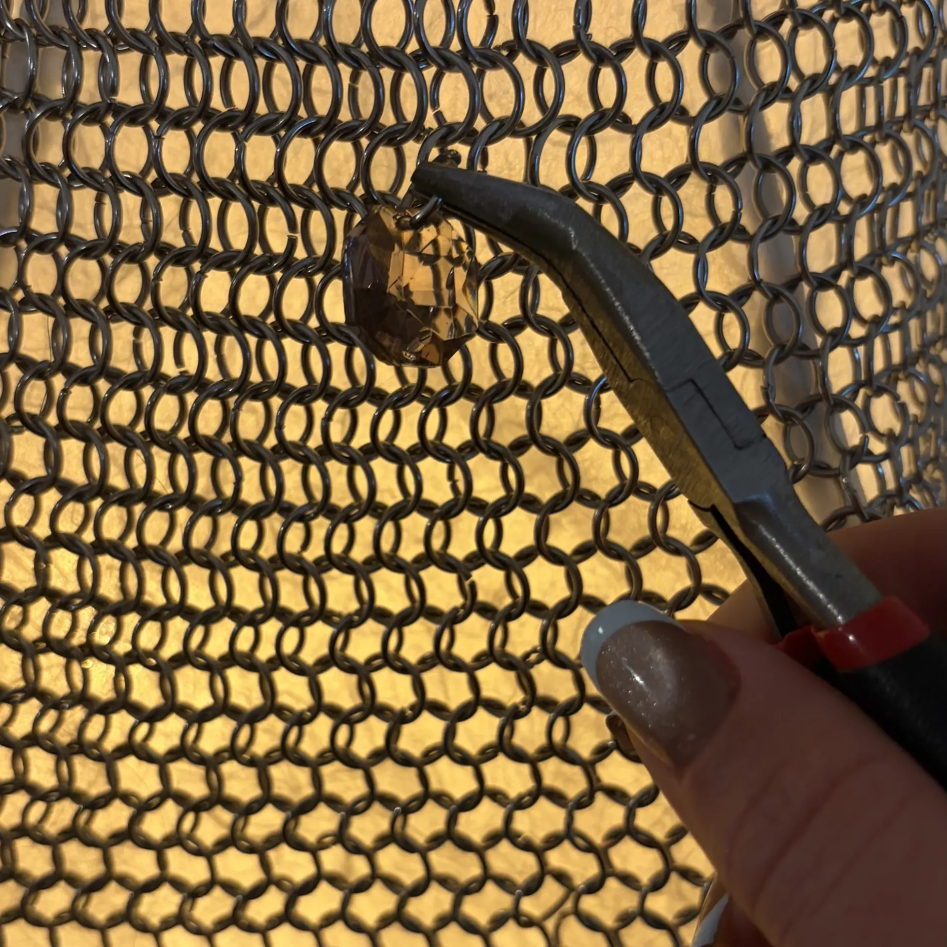 A hand using pliers to set a single crystal into the chainmail.